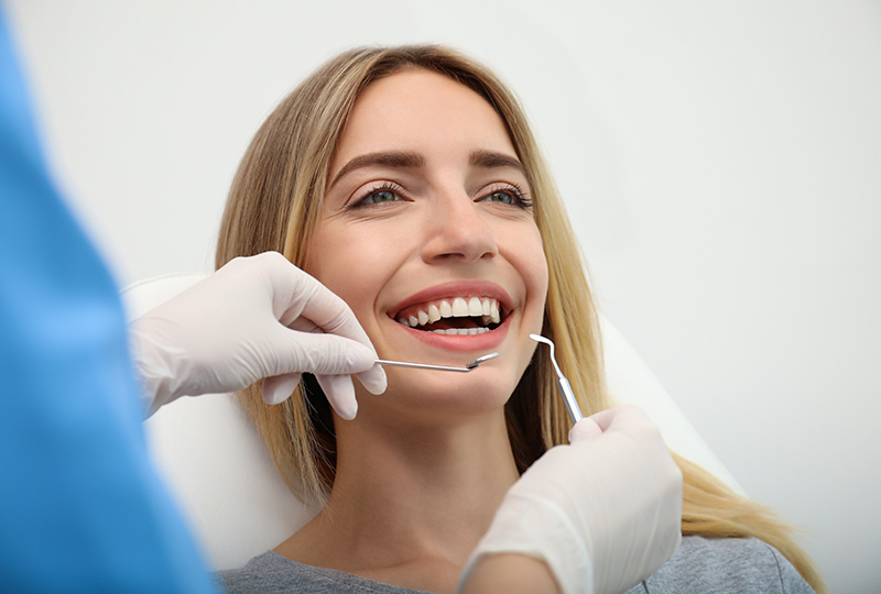 A woman seated in a dental chair receiving dental treatment with a smiling expression, surrounded by medical professionals.